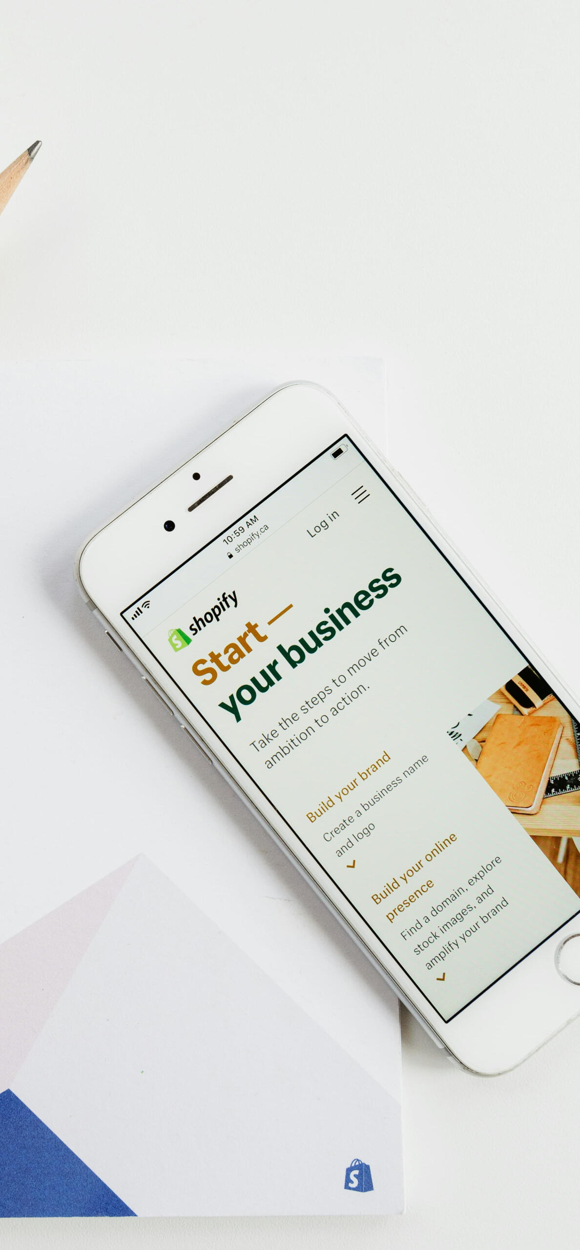Smartphone displaying Shopify's 'Start your business' screen next to a notebook and pencil, capturing the planning stage of building a Shopify store.