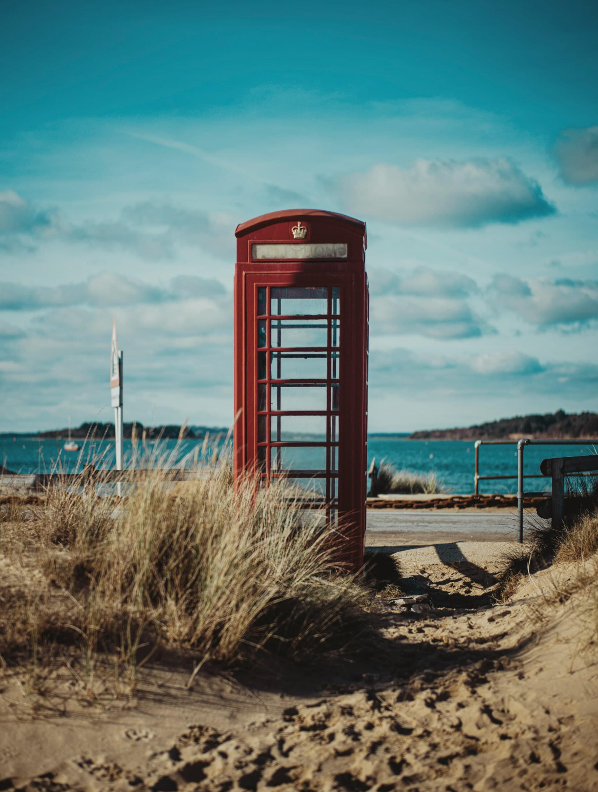 Red British phone box on a quiet UK beach path, symbolising independent local connection and open communication with Vendora.